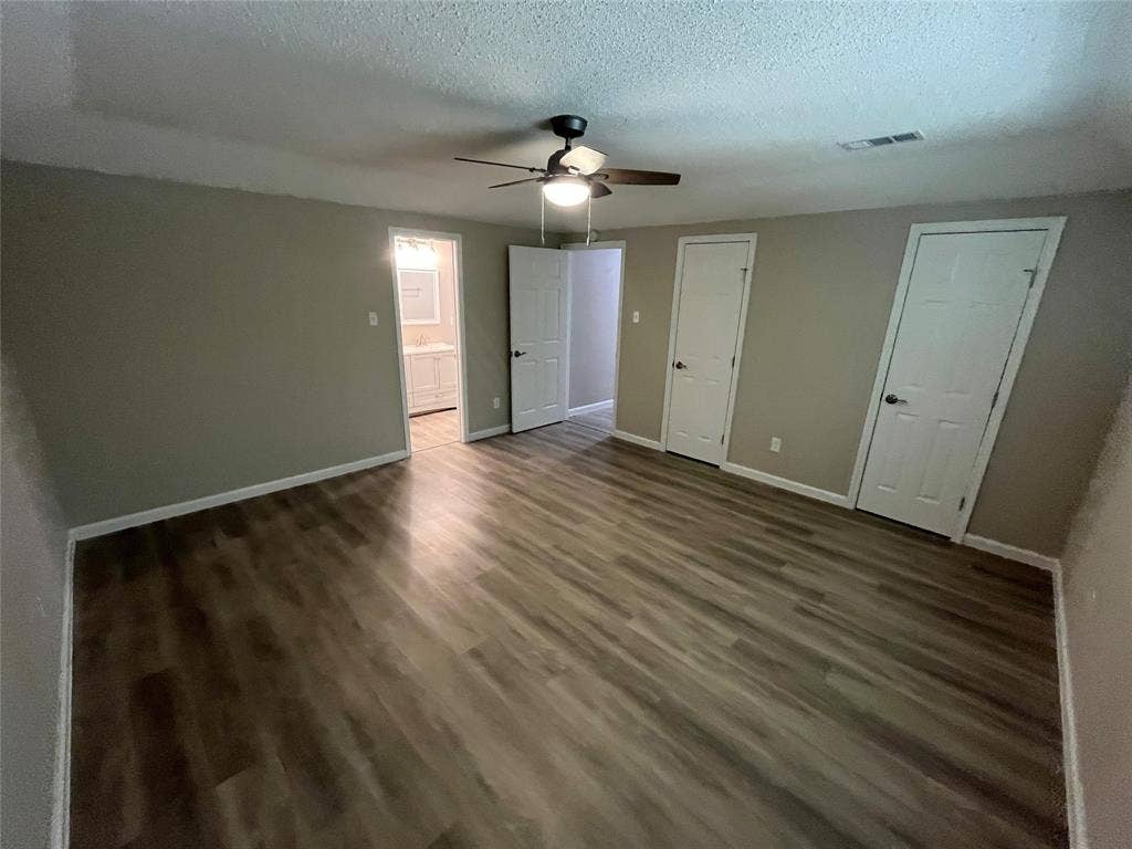 Spacious room with wood-finish flooring, neutral wall tones, and a ceiling fan