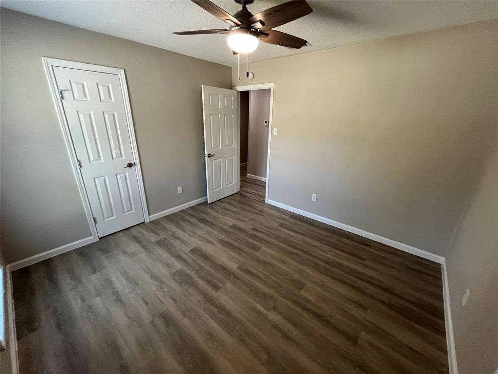 Wood-finish flooring, neutral wall tones, white paneled doors, and a ceiling fan with integrated lighting