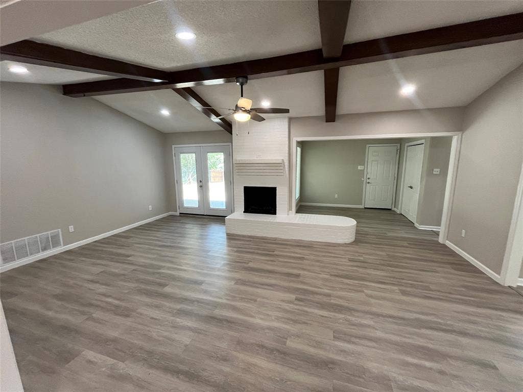 Vaulted ceiling with exposed wood beams, recessed lighting, wood-finish flooring, white brick fireplace with hearth, and French doors