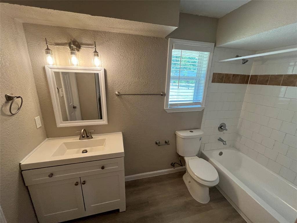 White vanity with integrated sink, brushed nickel fixtures, subway tile bath surround with accent band, and wood-finish flooring