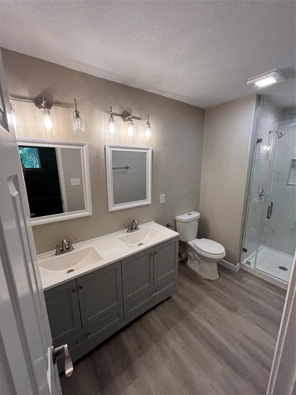 Dual vanity with integrated sinks, brushed nickel fixtures, wood-finish flooring, and a glass-enclosed shower