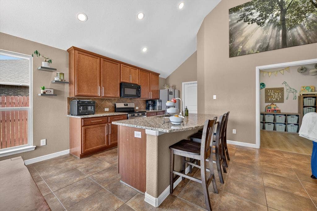 424 Foxcraft Drive, Fort Worth, TX 76131 Kitchen featuring a vaulted ceiling, recessed lighting, wood cabinetry, stone countertops, and tile flooring