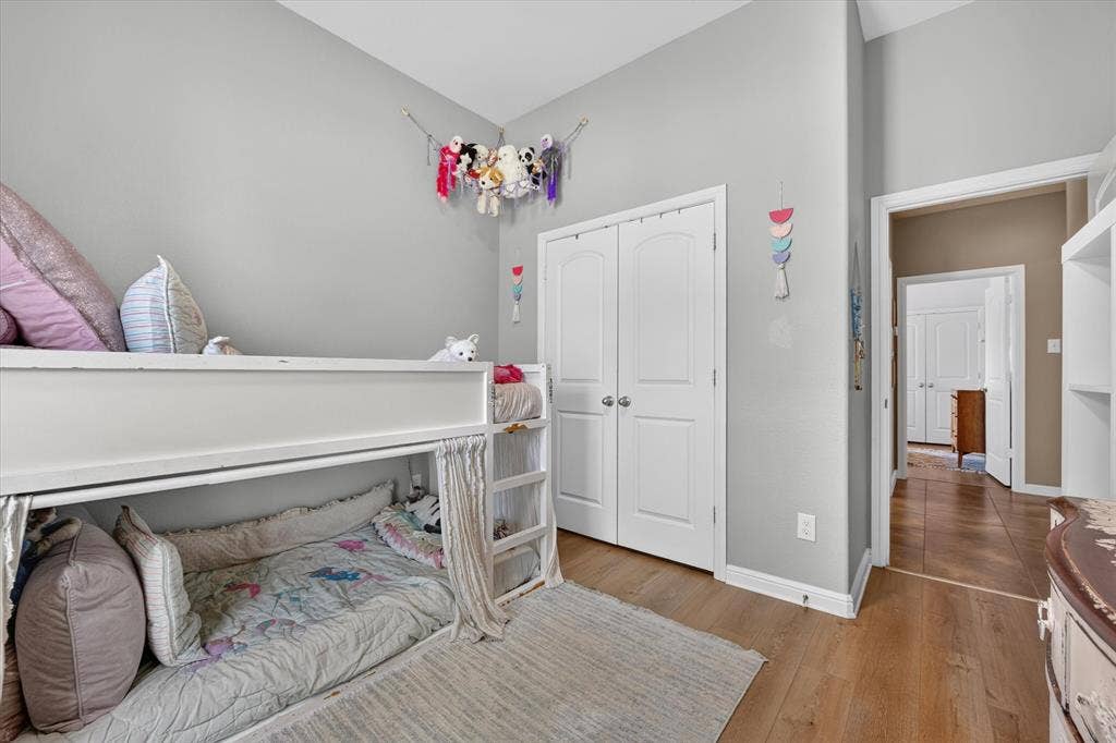 424 Foxcraft Drive, Fort Worth, TX 76131 Bright bedroom featuring hardwood flooring, built-in lofted bed with storage underneath, dual closets with white six-panel doors, and soft neutral wall finishes