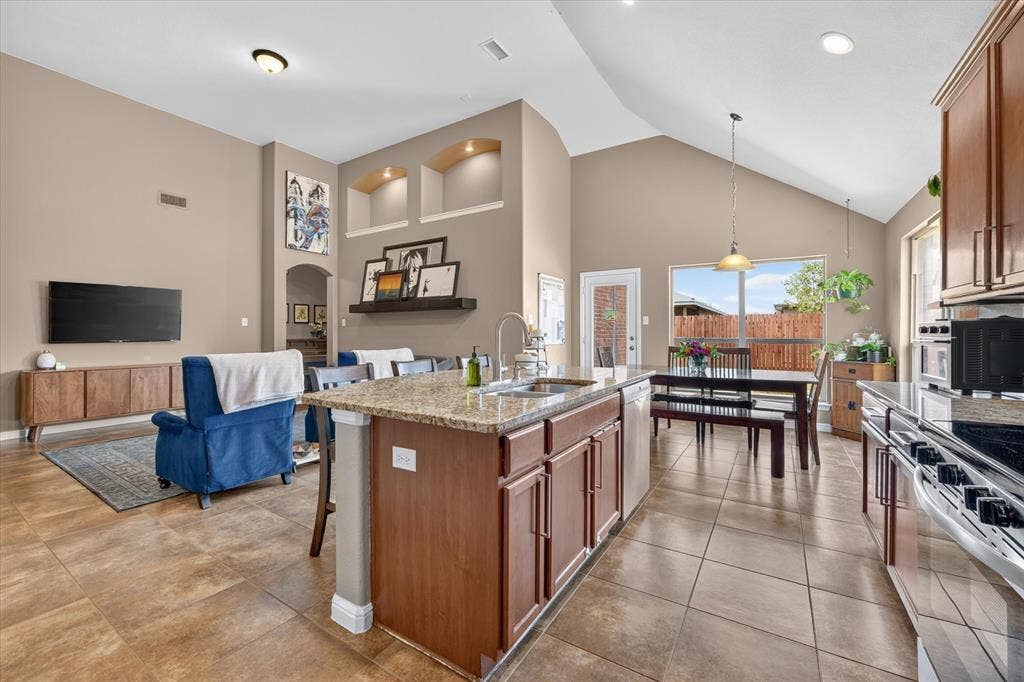 424 Foxcraft Drive, Fort Worth, TX 76131 Open-concept living space featuring vaulted ceilings, tile flooring, a kitchen island with stone countertop, and built-in display niches