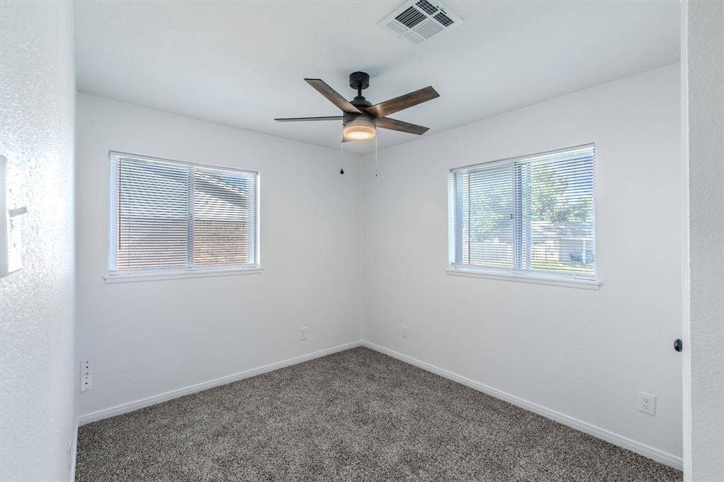 4133 Sherry Lane, Beverly Hills, TX 76711 Two windows with blinds, wood-finish ceiling fan with integrated lighting, textured white walls, and gray carpet