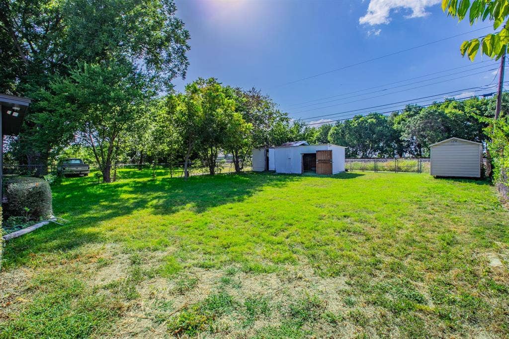 4133 Sherry Lane, Beverly Hills, TX 76711 Expansive fenced yard with mature trees, two storage sheds, and a chain-link perimeter