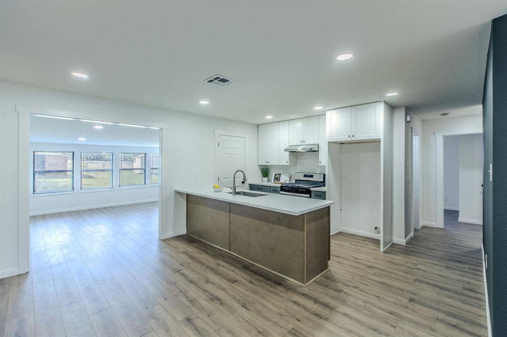 4133 Sherry Lane, Beverly Hills, TX 76711 Modern open-concept kitchen and living area featuring a wood-finish plank floor, stainless steel appliances, white cabinetry, a large island with wood-finish base and countertop seating, recessed lighting, and abundant natural light from multi-pane windows