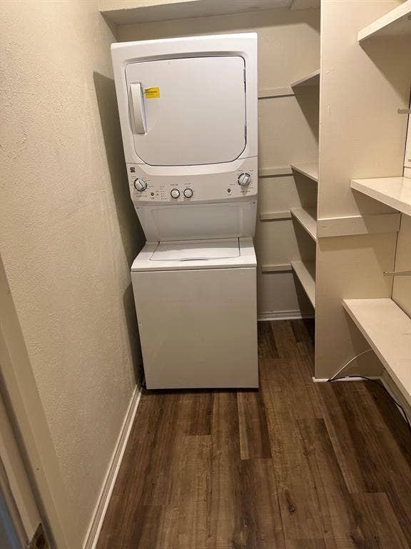 6050 Birchbrook Drive, #242, Dallas, TX 75206 Compact laundry area featuring a stacked washer and dryer, wood-finish flooring, and built-in shelving