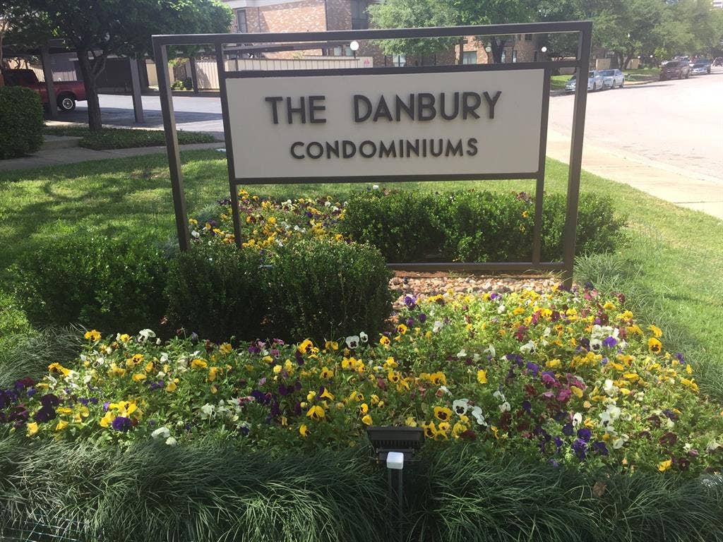 6050 Birchbrook Drive, #242, Dallas, TX 75206 Entrance signage with a dark-framed design, set within a landscaped bed featuring diverse flowering plants and manicured shrubs