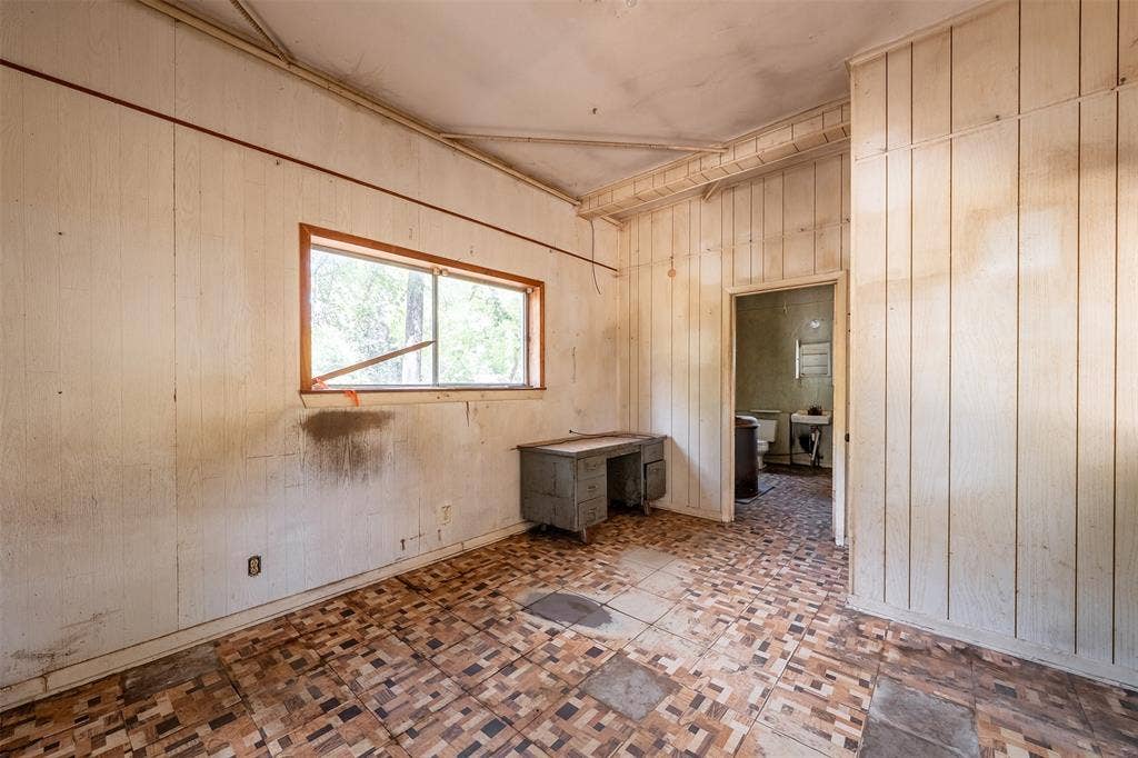 5250 Fm 2494, Athens, TX 75751 Spacious interior room featuring original wood-finish flooring in a classic brick pattern, wood-paneled walls, and a large fixed window with wood framing that provides natural light