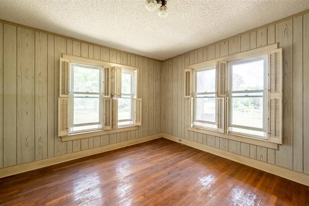 5250 Fm 2494, Athens, TX 75751 Wood-finish flooring with a sheen, vertical wood paneling, multiple windows with interior shutters, and a textured ceiling