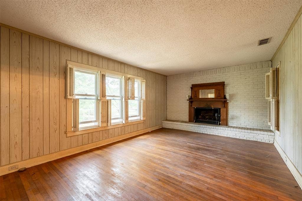 5250 Fm 2494, Athens, TX 75751 Wood-finish flooring, white painted brick fireplace with a wood mantel, multiple windows with shutters, and wood-paneled walls