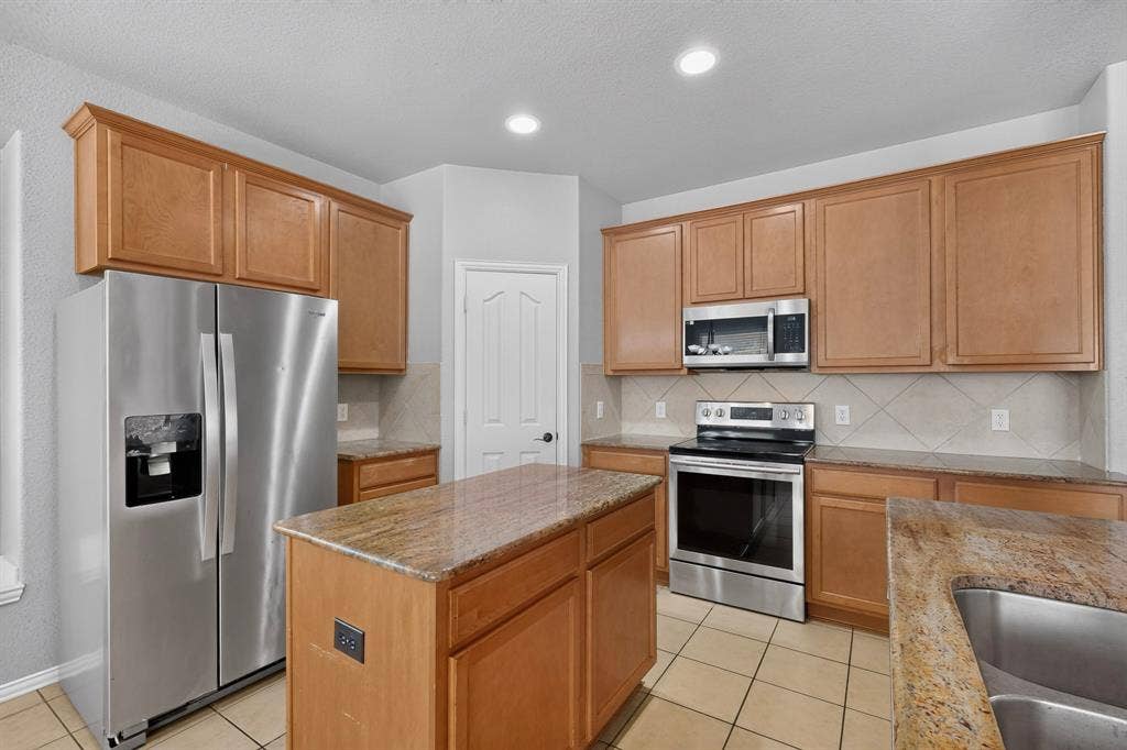 Kitchen featuring wood cabinetry, stainless steel appliances, granite countertops, tile backsplash, and a central island