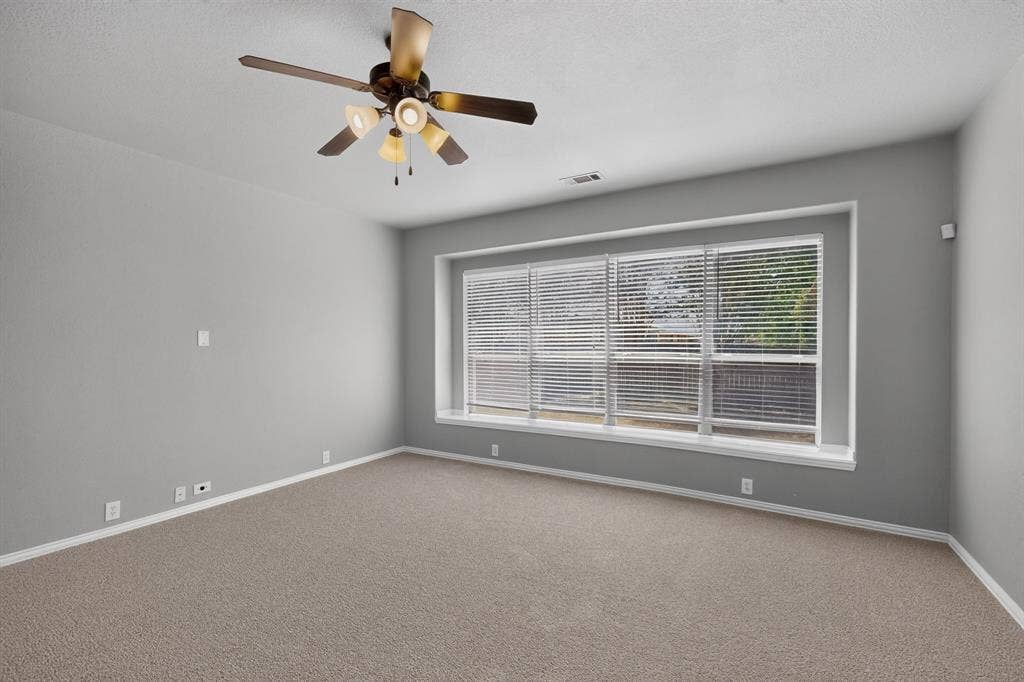 Neutral wall paint, plush carpeting, a large window with blinds, and a ceiling fan with integrated lighting