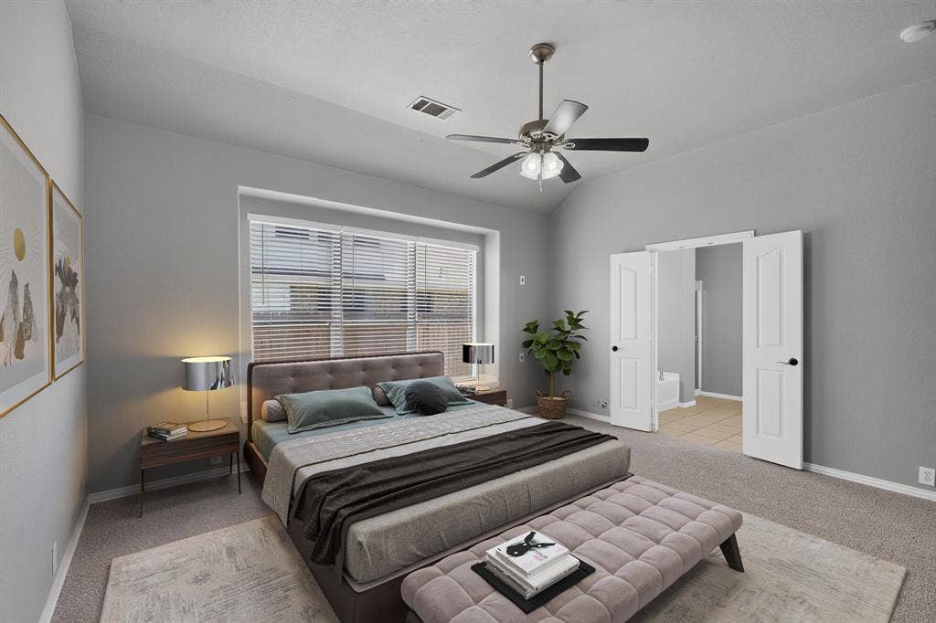 Spacious primary bedroom featuring a wood-finish platform bed, neutral carpeting, and abundant natural light from large windows with horizontal blinds