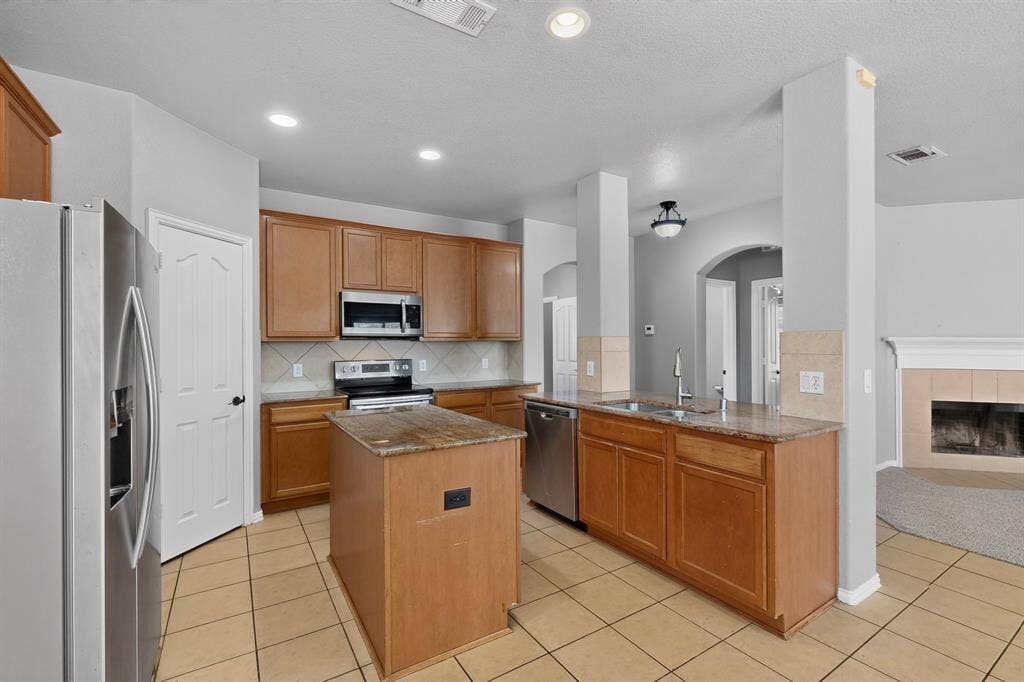 Kitchen featuring wood cabinetry, a center island with countertop, stainless steel appliances, and tile flooring
