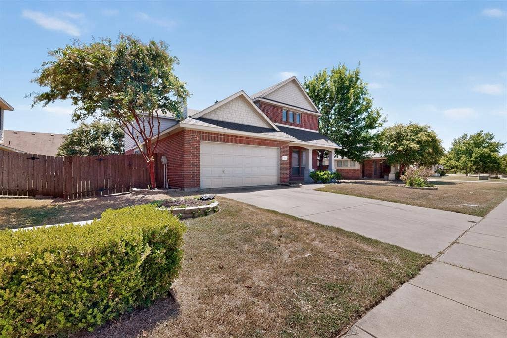 Brick and siding exterior with an attached garage, concrete driveway, and established landscaping