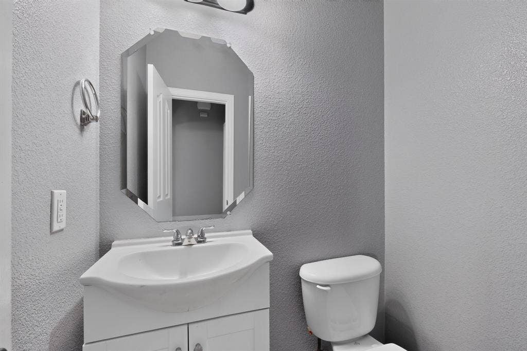 White vanity with integrated sink, chrome-finish faucet, and a decorative octagonal mirror