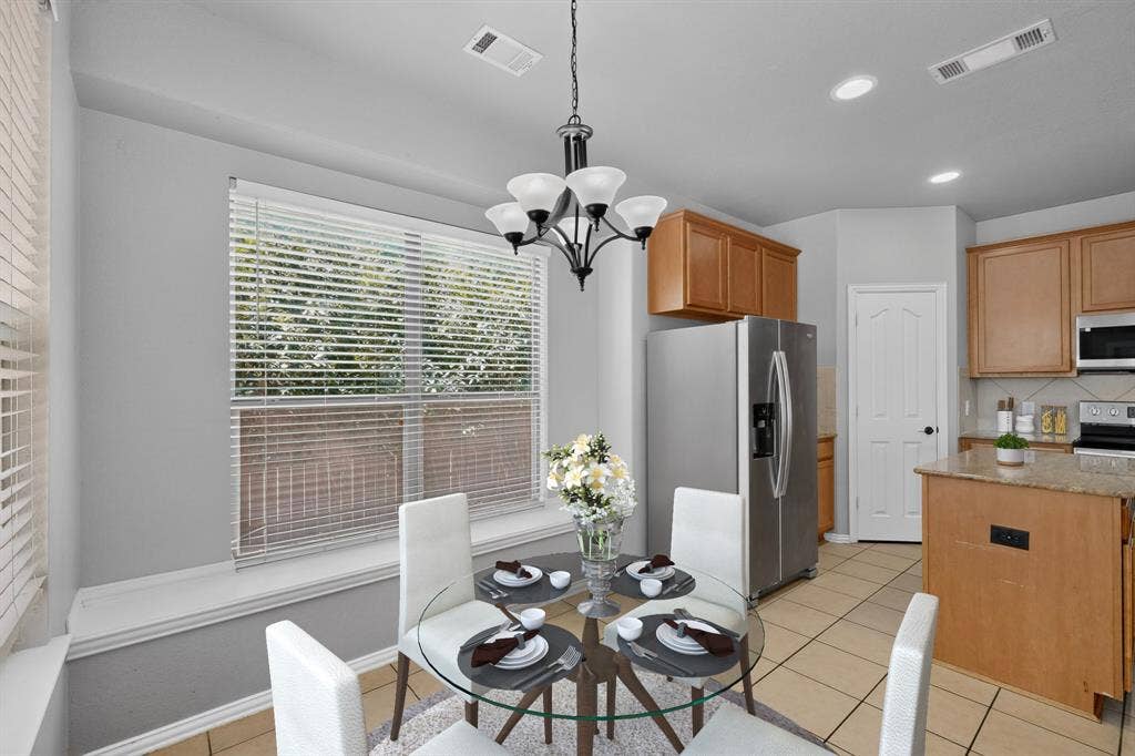 Recessed lighting, chandelier, wood-finish cabinetry, stainless steel refrigerator, and tiled flooring