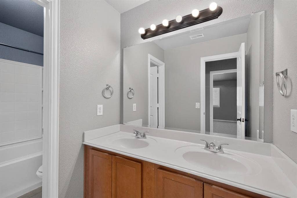 Dual sink vanity with wood-finish cabinetry and a single expansive mirror