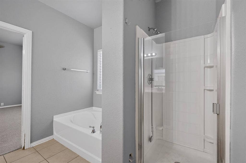 Tiled flooring, built-in bathtub with deck-mounted faucet, and glass-enclosed shower with a handheld shower fixture