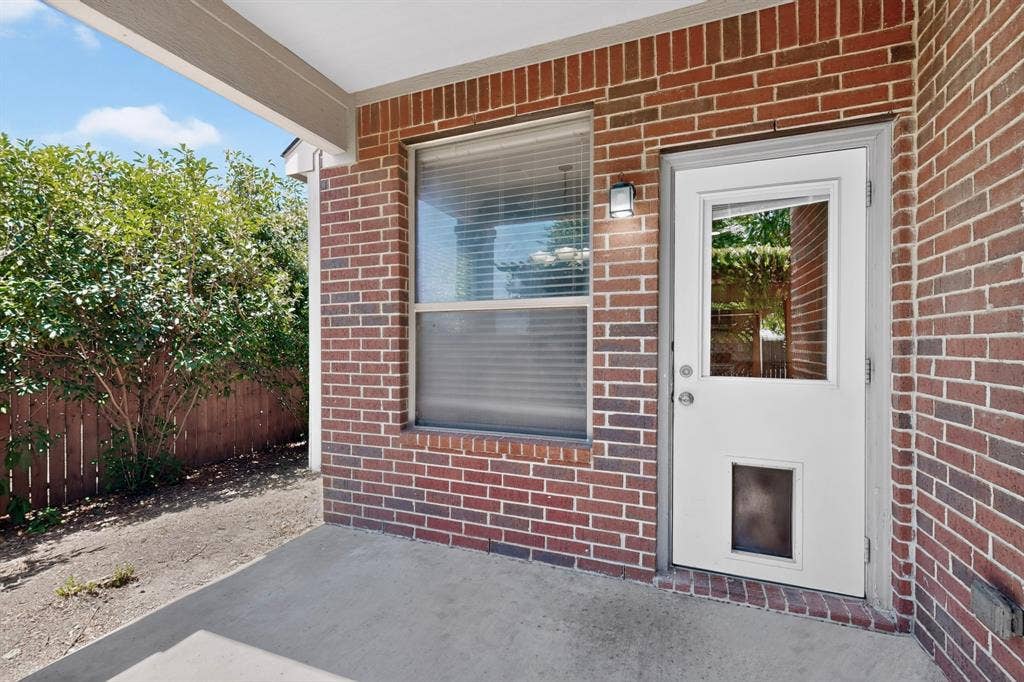 Covered concrete patio with a brick exterior, privacy fencing, and exterior lighting