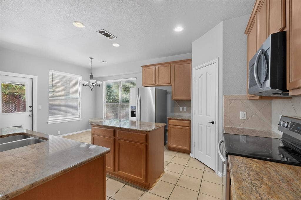 Kitchen featuring light wood-finish cabinetry, granite countertops, stainless steel appliances, and tile flooring