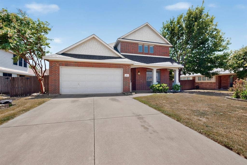 Brick exterior with white trim, attached two-car garage, concrete driveway, and covered front entry