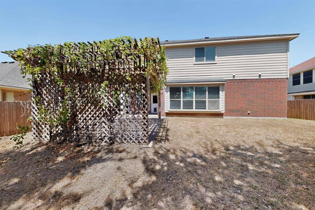 Private backyard featuring a latticework pergola, mature landscaping, and a bay window