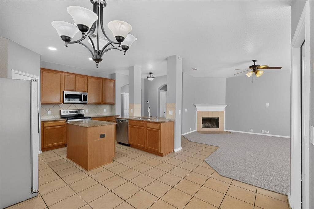 Kitchen featuring stainless steel appliances, wood-finish cabinetry, a central island with a granite-style countertop, and tile flooring