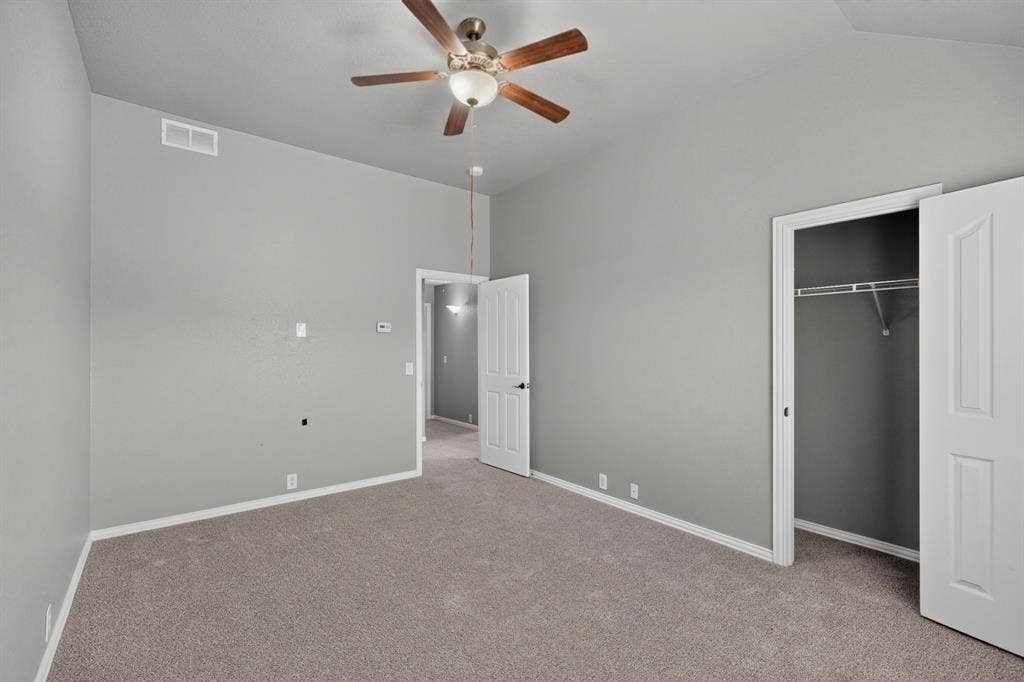 Vaulted ceiling with a ceiling fan, neutral gray wall paint, light gray carpet, and a white bi-fold closet door