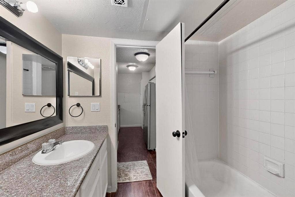 Bathroom featuring a vanity with an integrated sink, a dark framed mirror, and a tiled shower with a built-in tub