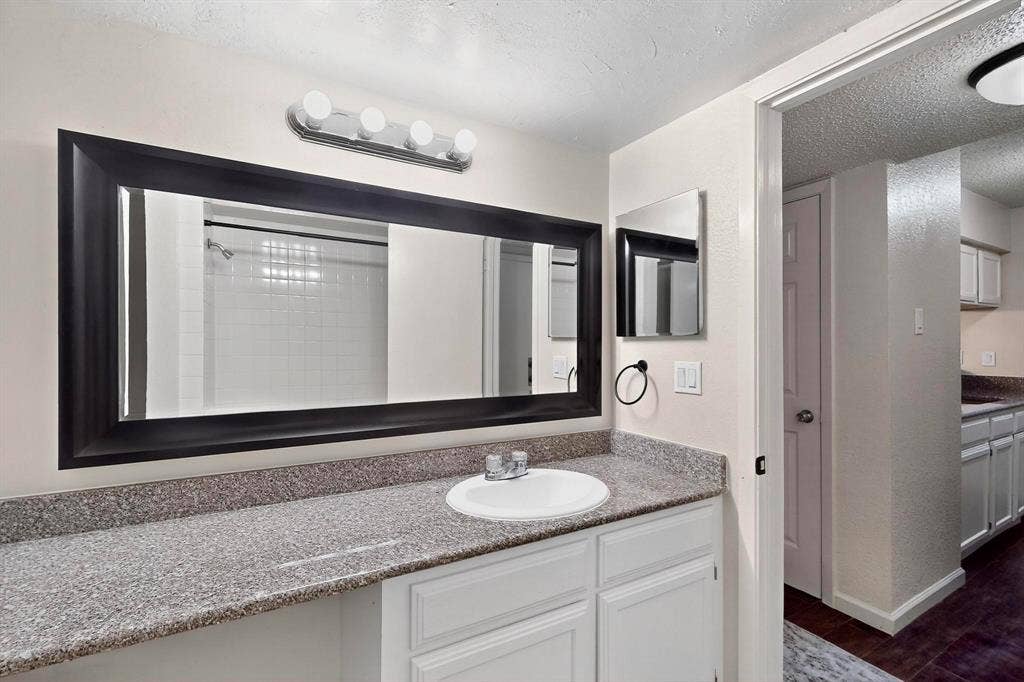 Spacious vanity with a composite countertop, an integrated sink, a large framed mirror, and a four-light fixture