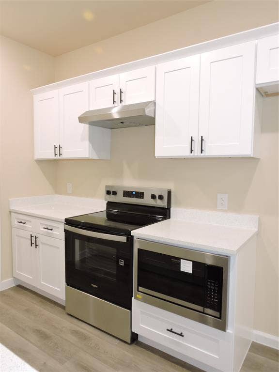 106 Navajo Drive, Mabank, TX 75156 White shaker-style cabinetry with black hardware, stainless steel range with overhead hood, stainless steel built-in microwave, white countertops, and wood-finish flooring