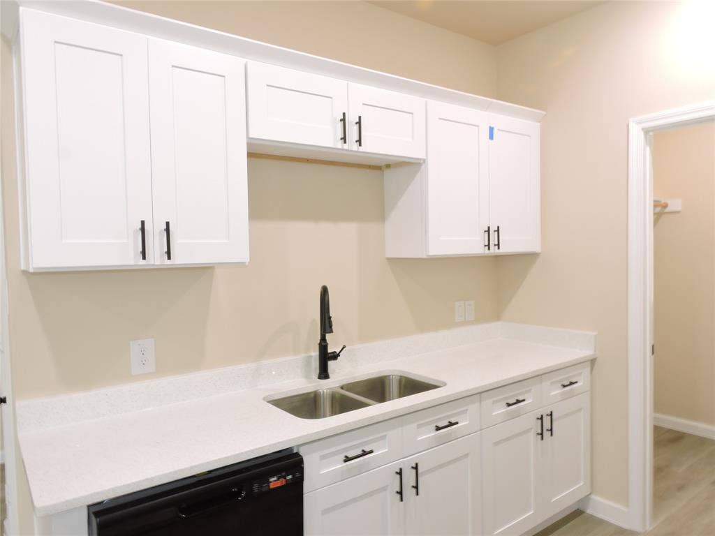 106 Navajo Drive, Mabank, TX 75156 White shaker-style cabinetry with matte black hardware, dual-basin stainless steel sink with a black gooseneck faucet, light-toned countertop, and a built-in black dishwasher