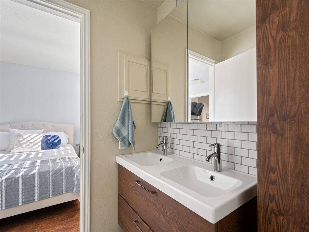 6220 Bentwood Trail, #205, Dallas, TX 75252 Dual rectangular undermount sinks, wood-finish vanity with two drawers, subway tile backsplash, and mirrored medicine cabinet