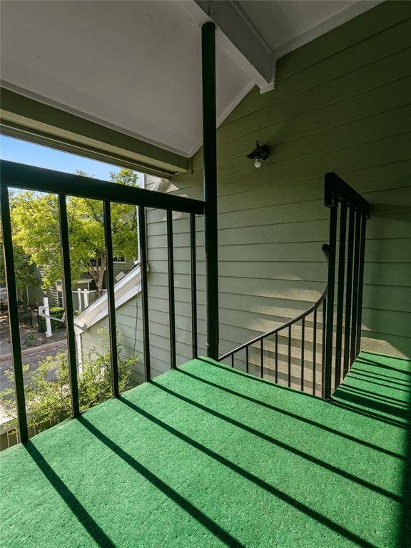 6220 Bentwood Trail, #205, Dallas, TX 75252 Balcony featuring green outdoor carpeting, black metal railings, and a wall-mounted light fixture