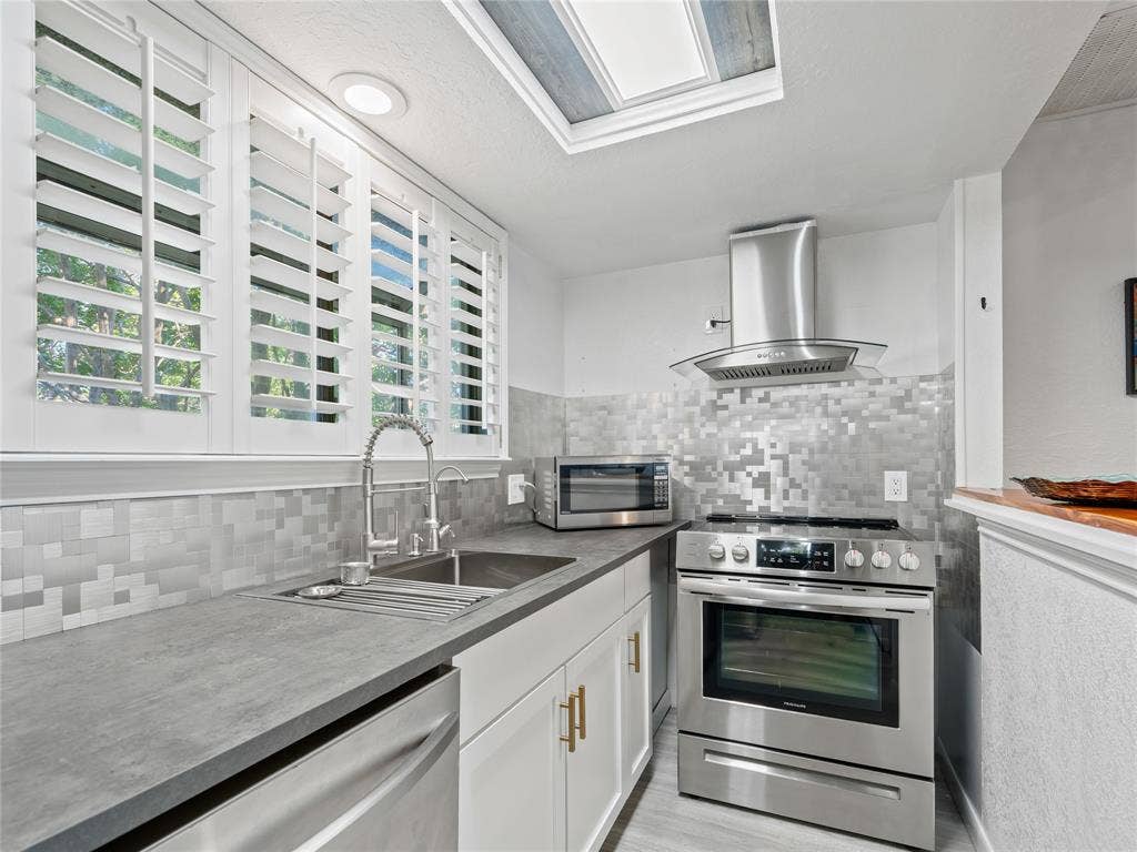 6220 Bentwood Trail, #205, Dallas, TX 75252 Kitchen featuring stainless steel appliances, solid surface countertops, a mosaic tile backsplash, a skylight, and white plantation shutters