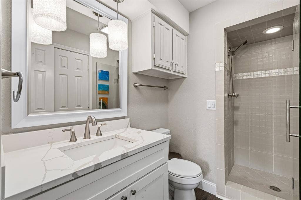 2705 Ithaca Court, Plano, TX 75025 White vanity with a rectangular undermount sink and a light-toned countertop, framed mirror with pendant lighting, and a walk-in shower with tiled walls and a glass door