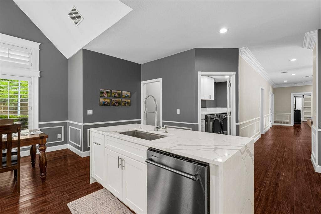 2705 Ithaca Court, Plano, TX 75025 Kitchen island with a built-in stainless steel sink and integrated dishwasher, hard-surface countertop, white cabinetry, and wood-finish flooring