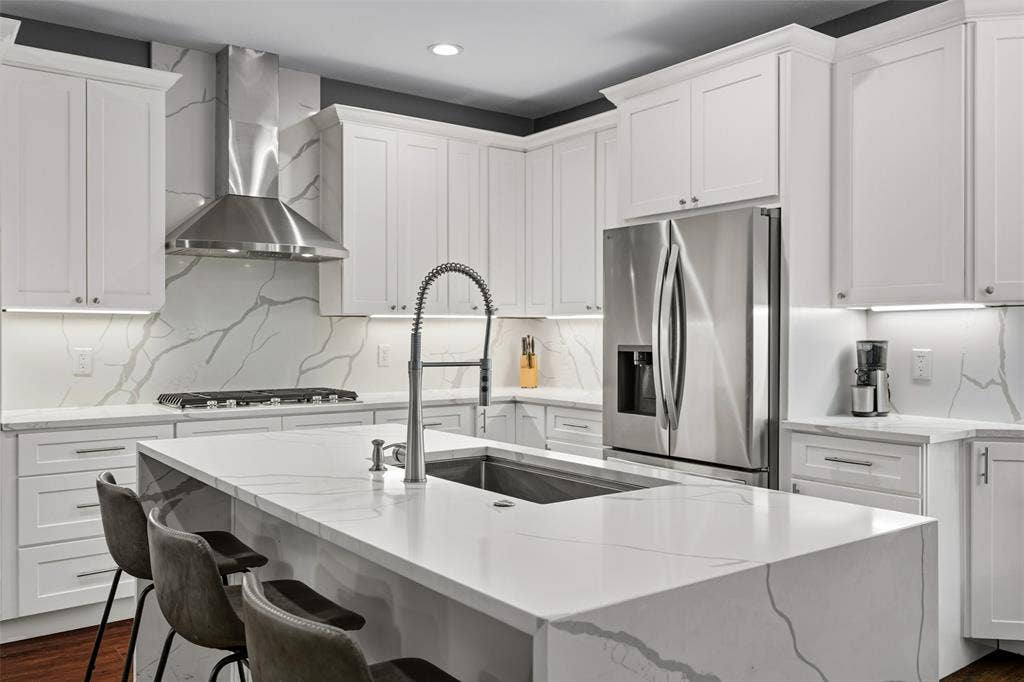 2705 Ithaca Court, Plano, TX 75025 Full kitchen featuring white shaker cabinetry, stainless steel appliances, a large center island with an integrated sink, and stone countertops with a matching backsplash