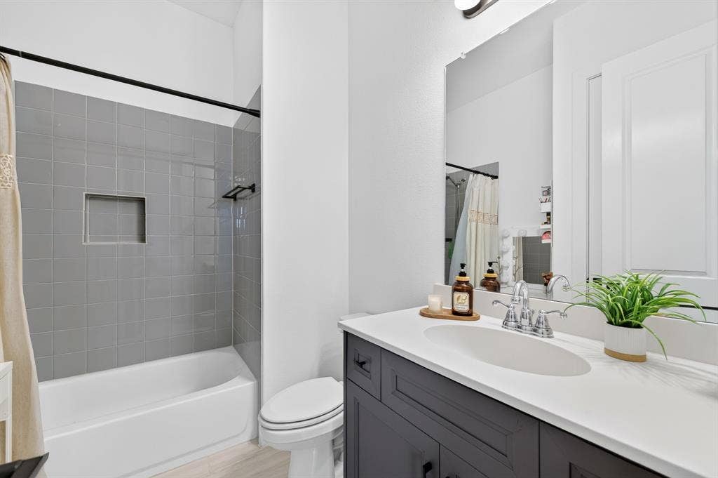 2809 Buckskin Lane, Northlake, TX 76247 Bathtub with gray tile surround and recessed niche, dark cabinetry with chrome hardware, integrated sink with chrome faucet, wall-mounted mirror, and wood-finish flooring