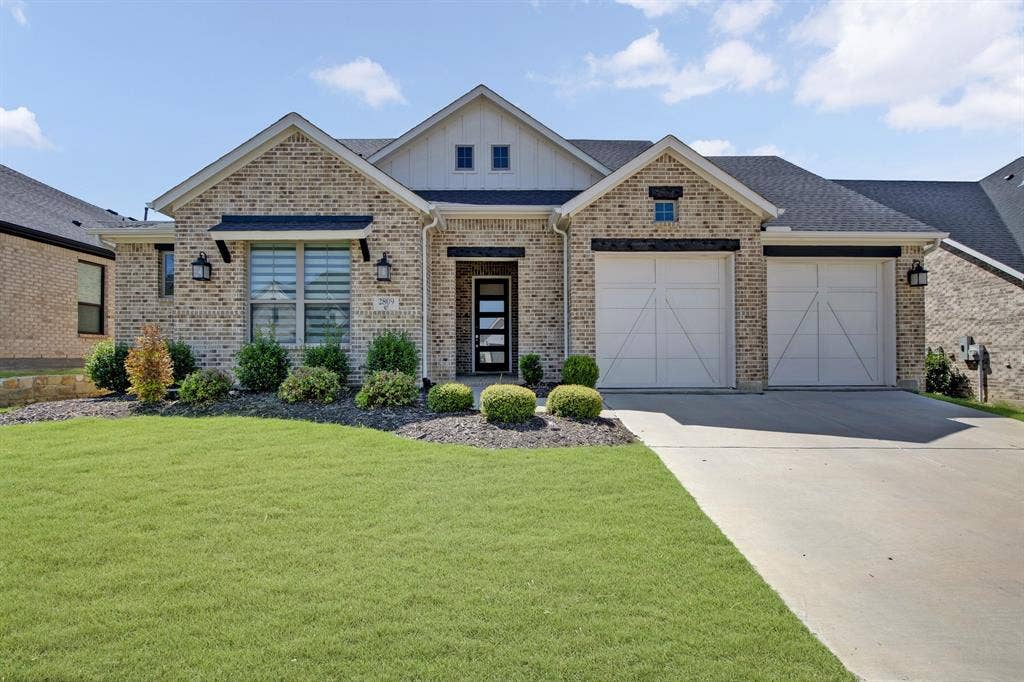 2809 Buckskin Lane, Northlake, TX 76247 Brick exterior with board-and-batten gables, a two-car garage with carriage-style doors, a concrete driveway, and mature landscaping