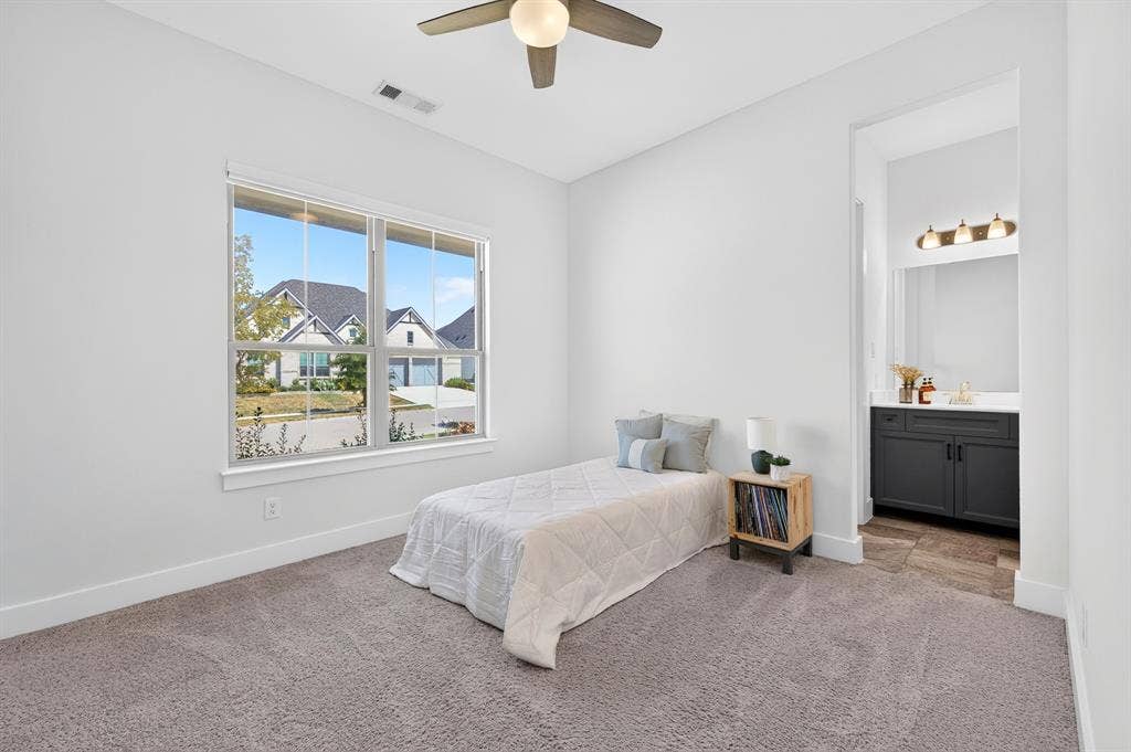 2809 Buckskin Lane, Northlake, TX 76247 Plush carpeted room featuring a large window, a ceiling fan, and access to a bathroom with a dark vanity, white countertop, and three-light fixture