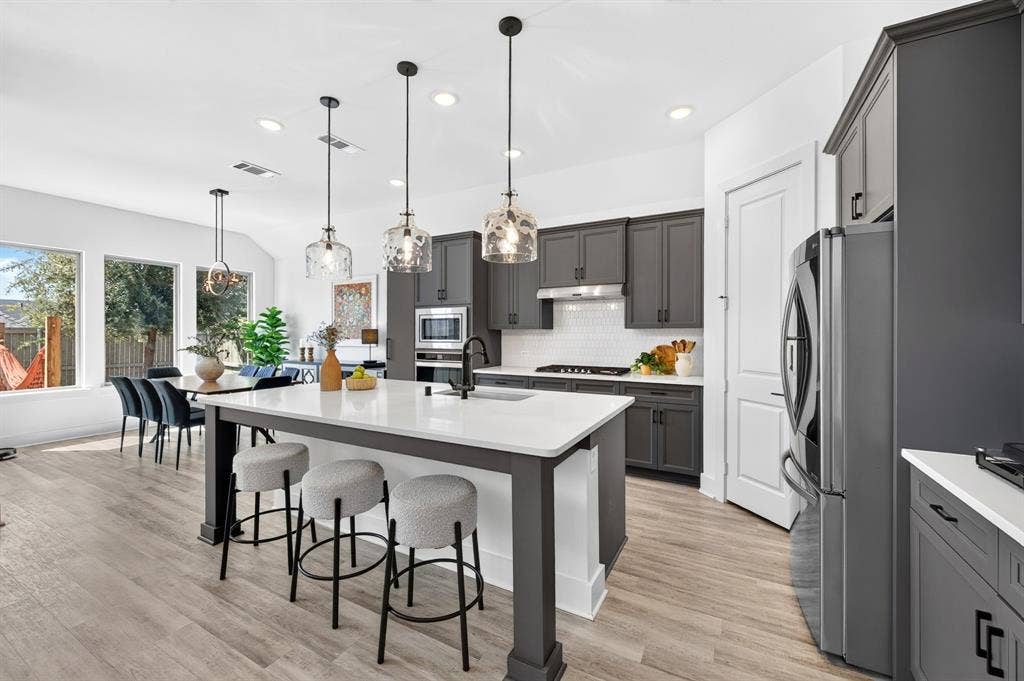2809 Buckskin Lane, Northlake, TX 76247 Open-concept kitchen with a large central island, dark gray cabinetry, stainless steel appliances, and wood-finish flooring