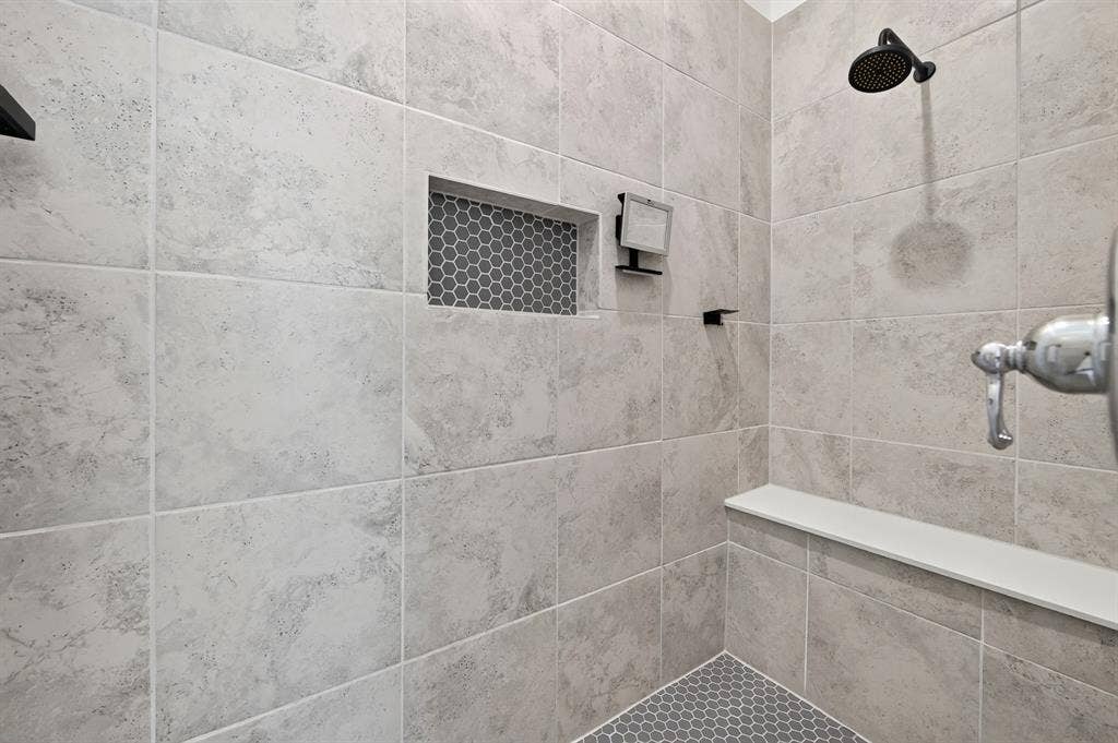 2809 Buckskin Lane, Northlake, TX 76247 Tiled shower with a built-in niche featuring hexagonal mosaic tile, a white shower bench, and a matte black rain shower head