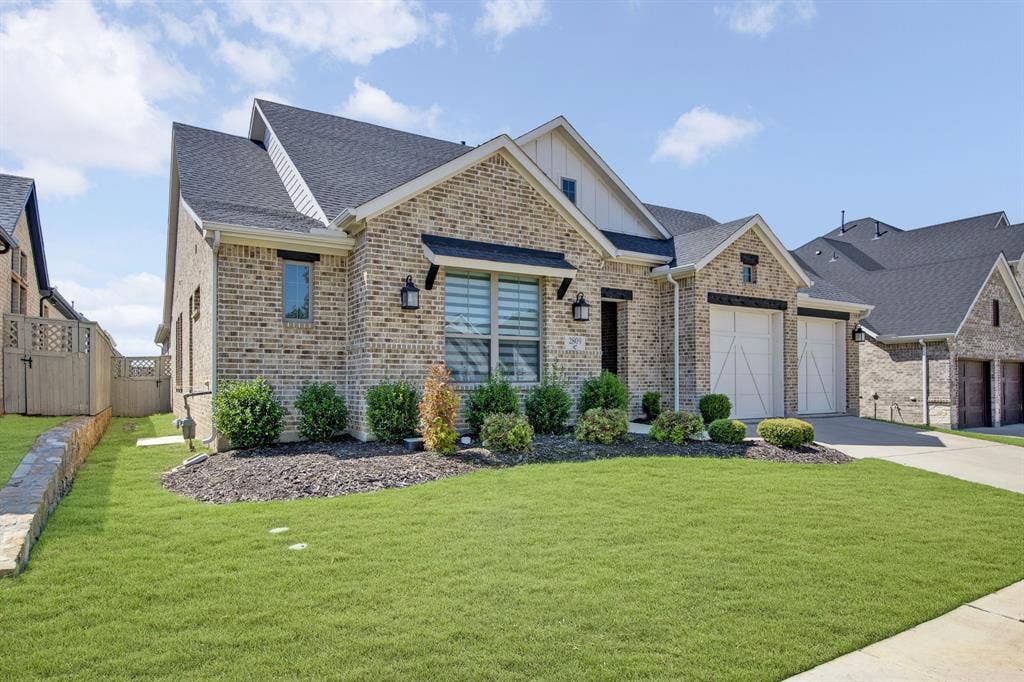 2809 Buckskin Lane, Northlake, TX 76247 Brick exterior with a dark shingle roof, two-car garage with carriage-style doors, landscaped front yard, and a paved driveway