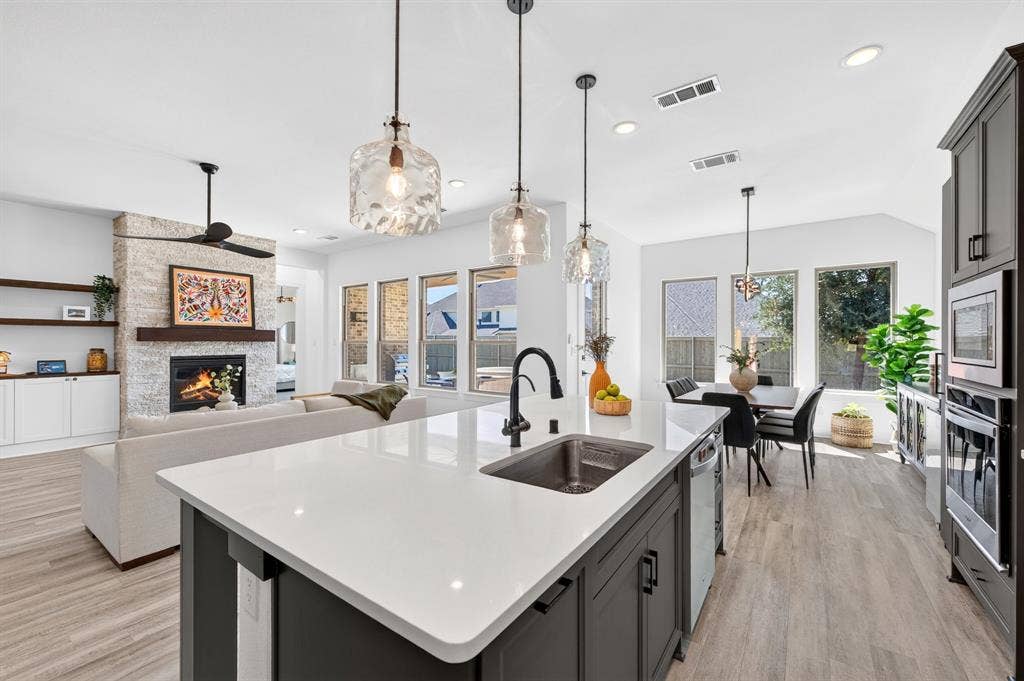 2809 Buckskin Lane, Northlake, TX 76247 Kitchen island with stone countertop and undermount sink, pendant lighting, wood-finish flooring, stone-clad fireplace with wood mantel, and built-in white cabinetry with shelving