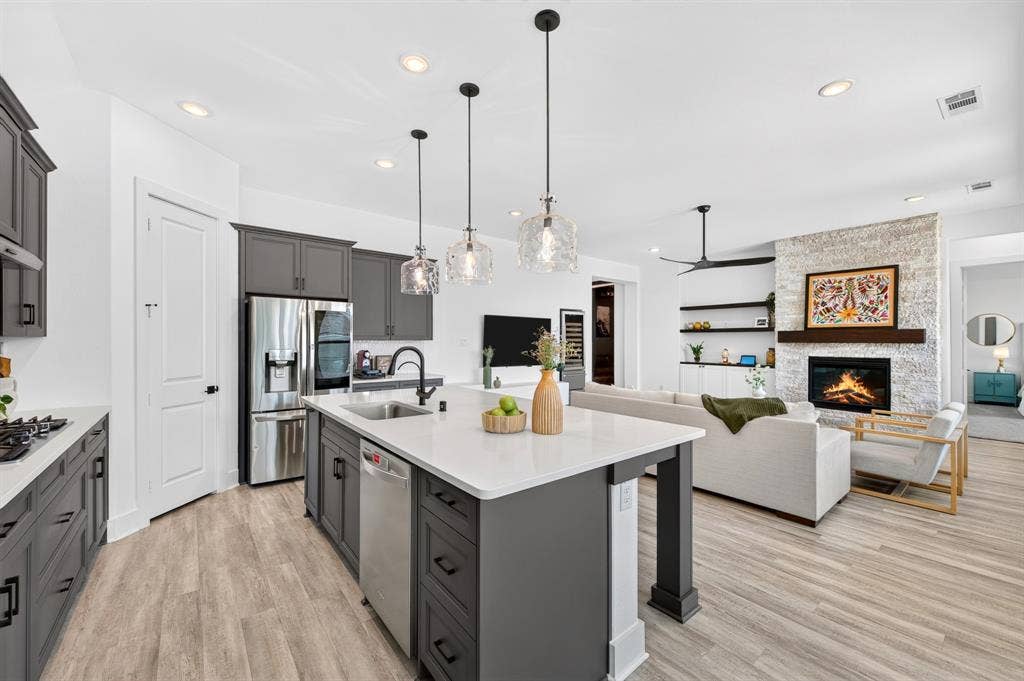 2809 Buckskin Lane, Northlake, TX 76247 Open-concept kitchen and living area featuring a stone fireplace, wood-finish flooring, recessed lighting, a kitchen island with pendant lighting, and stainless steel appliances