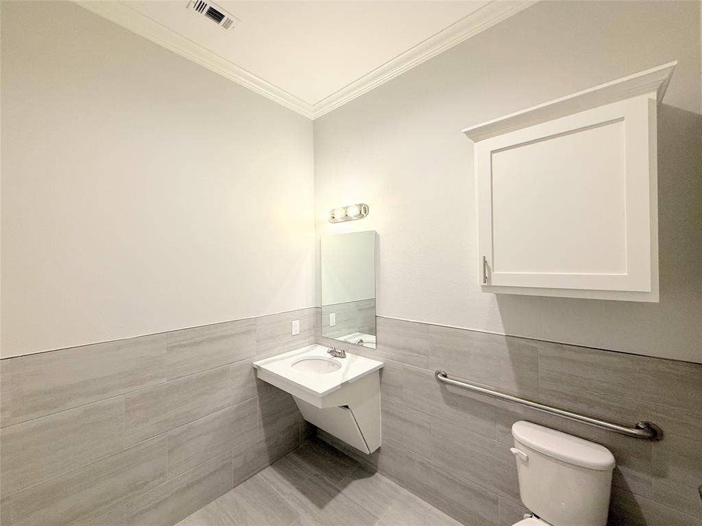 2120 Prairie Drive, #901, Prosper, TX 75078 Crown molding details, wall-mounted sink with built-in storage, light gray tiled walls, matching tiled flooring, and a wall-mounted white storage cabinet